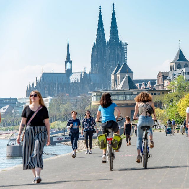 Mehrere Fußgängerinnen und Fußgänger teilen sich das schmale Konrad-Adenauer-Ufer in Köln, im Hintergrund ist die Bastei zu sehen.