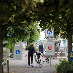 Zwei Radfahrer schieben ihre Räder auf der Rheinpromenade. Schilder weisen den Abschnitt in Höhe der Fähre als reine Fußgängerzone aus-