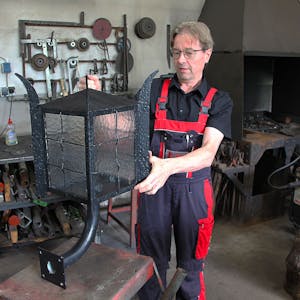 Das Bild zeigt Schmied Albert Köller in seiner Werkstatt. Er hat eine große Lampe in der Hand.