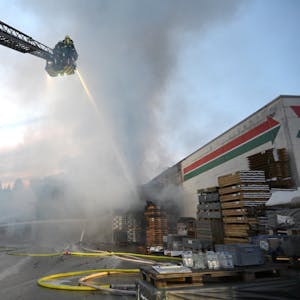 Ein Feuerwehrwagen steht vor einem brennenden Gebäude, auf der ausfahrbaren Leiter stehen Feuerwehrleute und kämpfen mit einem dicken Wasserstrahl gegen die Flammen.&nbsp;
