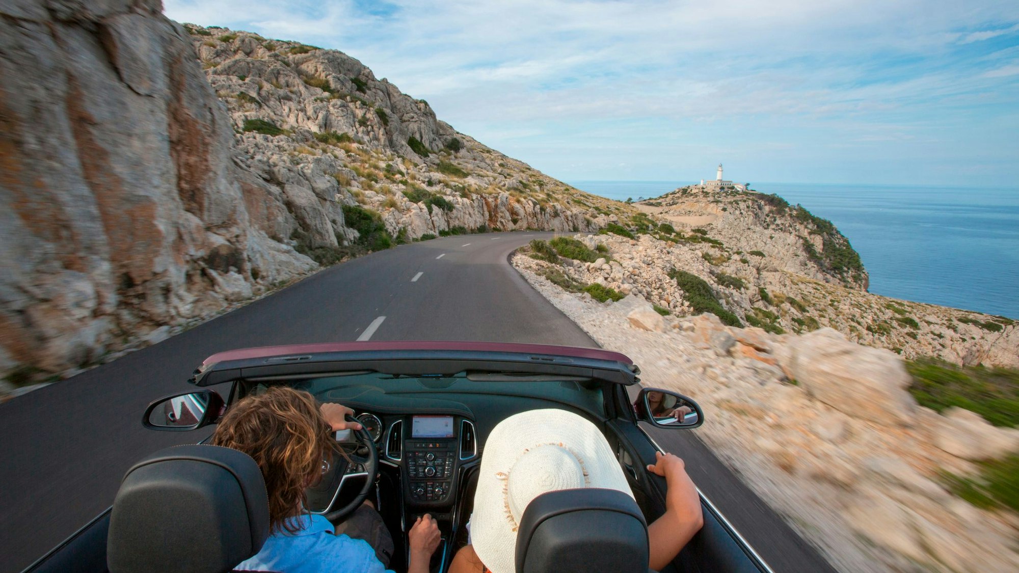 Ein Paar fährt in einem Cabrio auf einer Straße auf Mallorca.