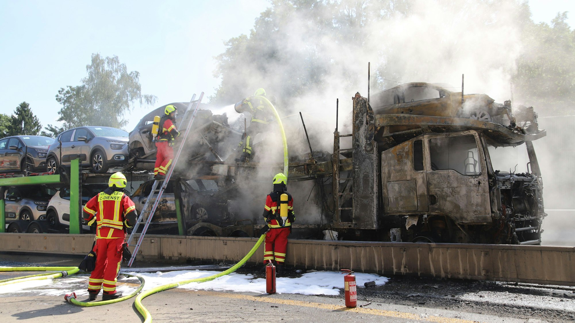 Feuerwehrleute löschen einen brennenden Autotransporter.