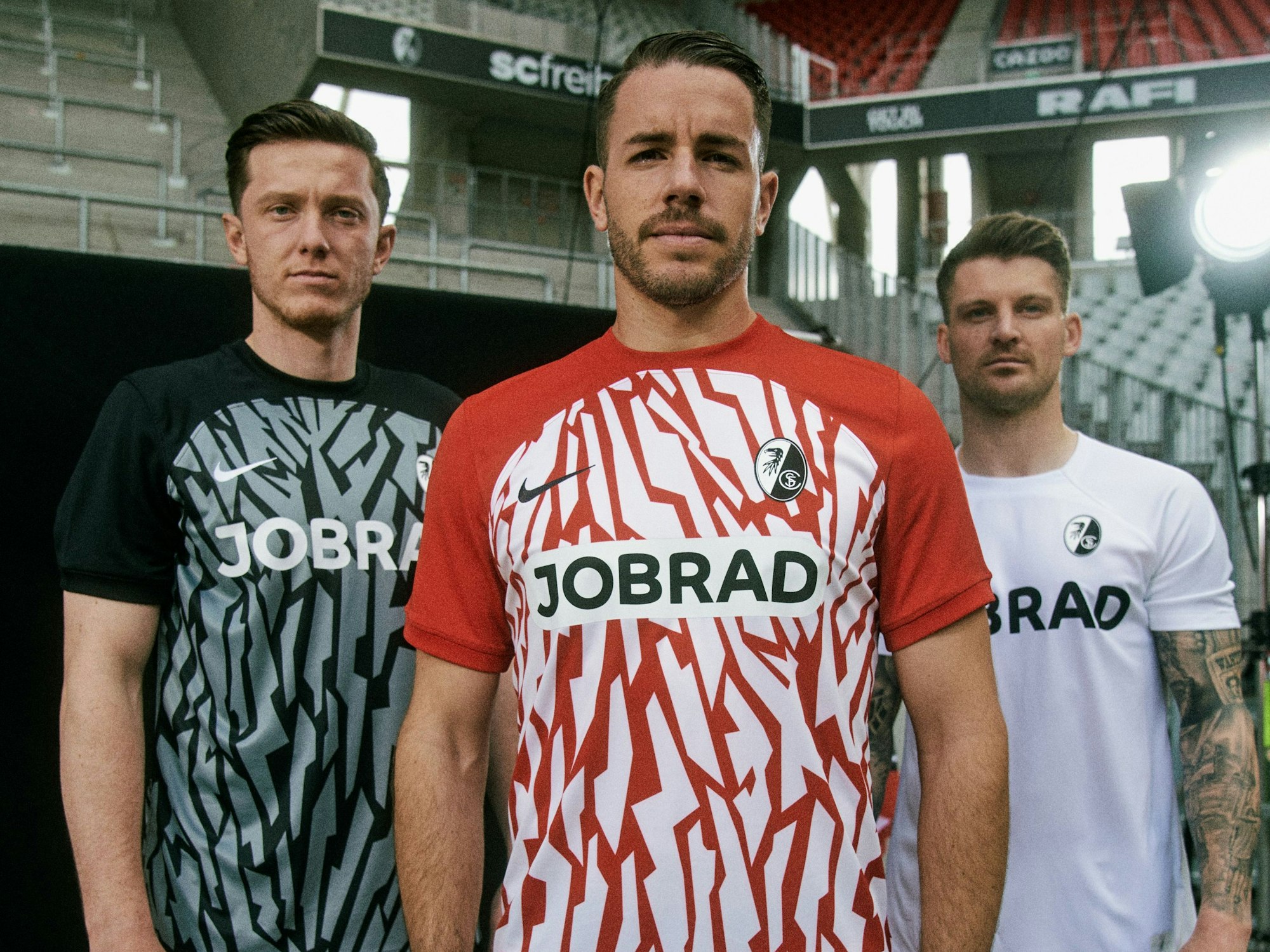 Spieler des SC Freiburg posieren mit den drei Trikots für die kommende Saison im Stadion.