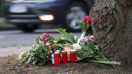 Blumen, Kerzen und Grablichter stehen am Straßenrand an einem Baum.