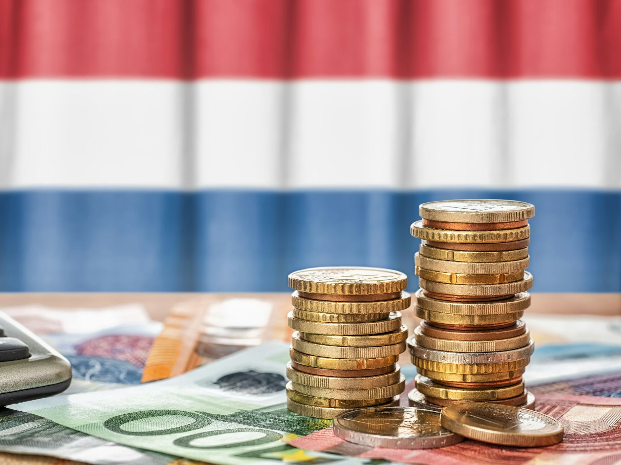 Euro Banknoten und Münzen liegen vor der niederländischen Flagge.