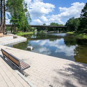 Zu sehen ist eine Sitzbank am Ufer des Teichs, im Hintergrund das neue Seecafé.