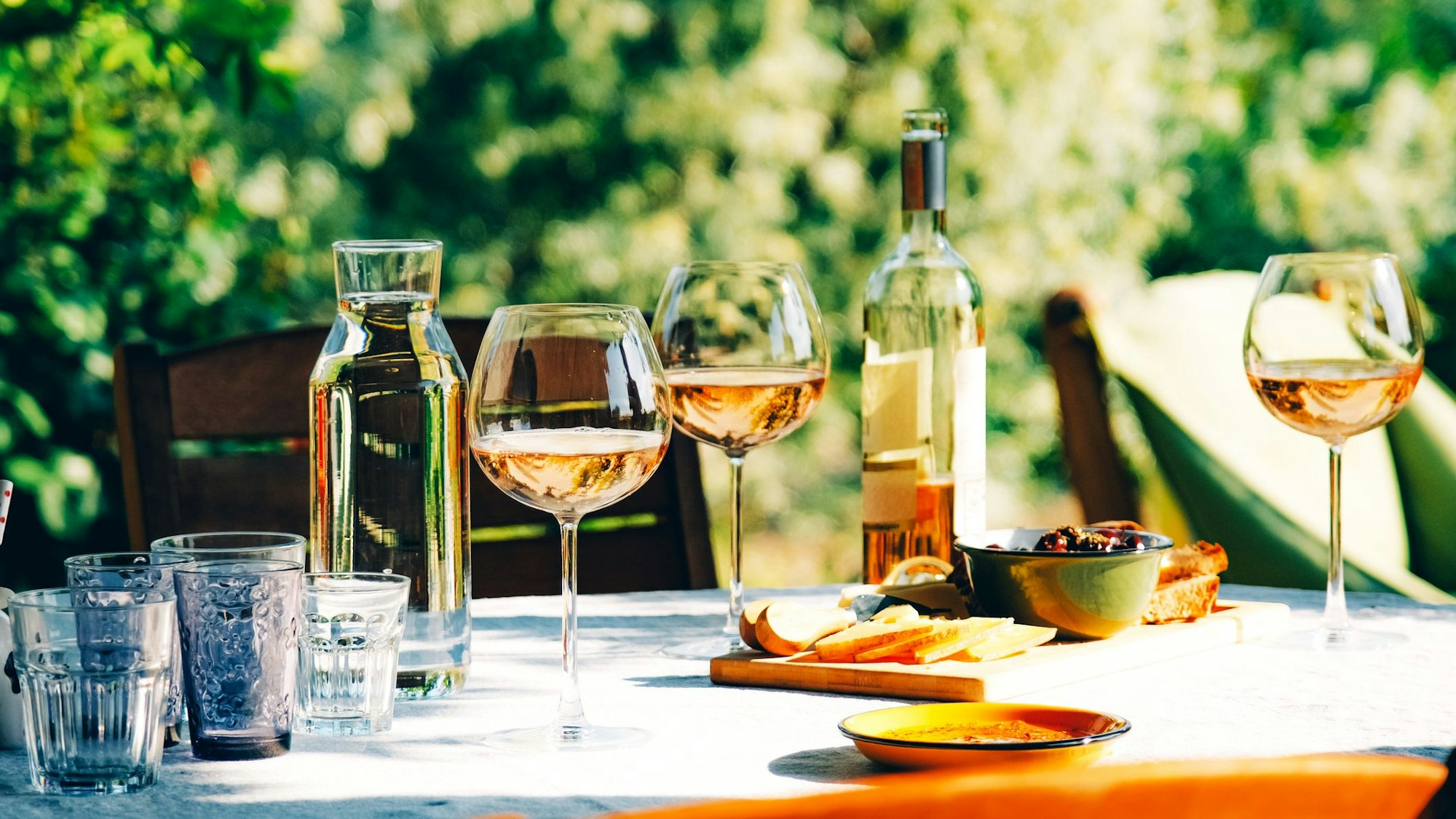 Roséwein im Glas und in der Flasche auf einem sommerlich gedeckten Tisch im Grünen