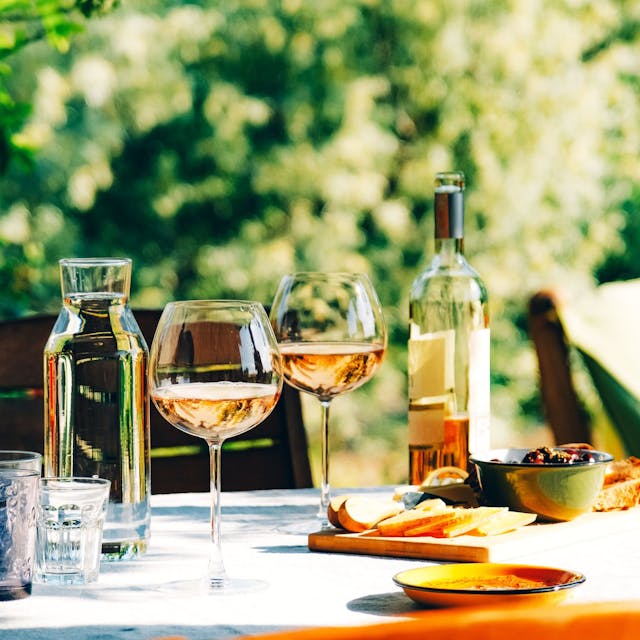 Roséwein im Glas und in der Flasche auf einem sommerlich gedeckten Tisch im Grünen