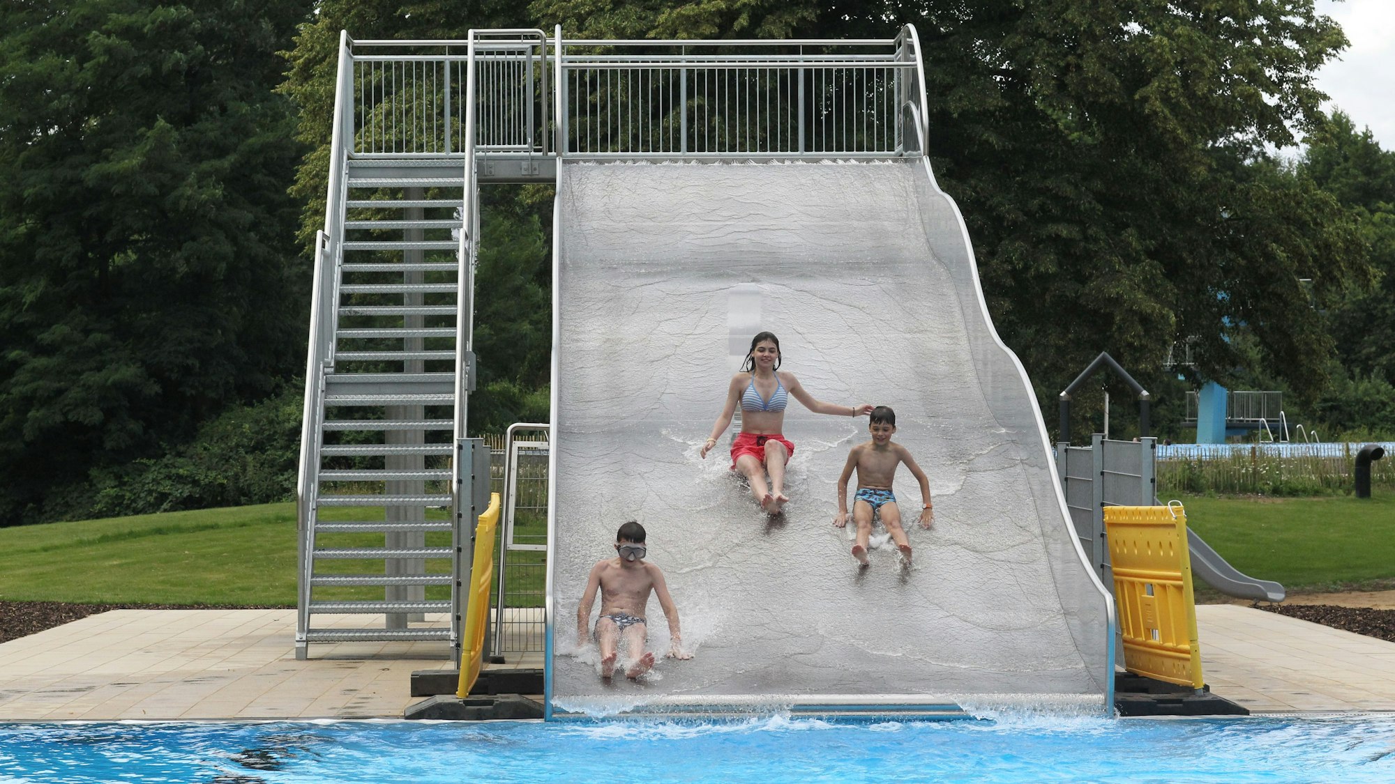 Drei Kinder rutschen eine Wasserrutsche in einem Schwimmbad herunter.