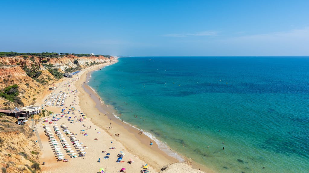 Sonnenliegen sowie Urlauberinnen und Urlauber in der Fig Tree Bay (Feigenbaumbucht) von Protaras auf Zypern. Sonnenliegen und Badegäste an der Praia da Falésia in Albufeira (Portugal). Der Strand zählt zu den besten preiswerten Stränden in Europa.