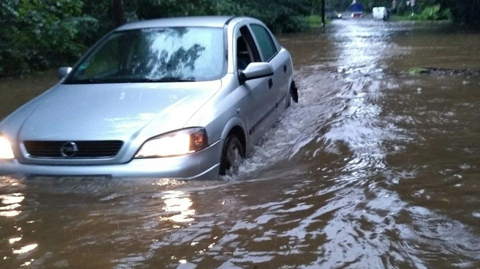 Ein Auto steckt im Hochwassers in Dünnwald fest. Die gesamte Straße ist voller Wasser, es steht dem Auto bis zu den Lichtern.