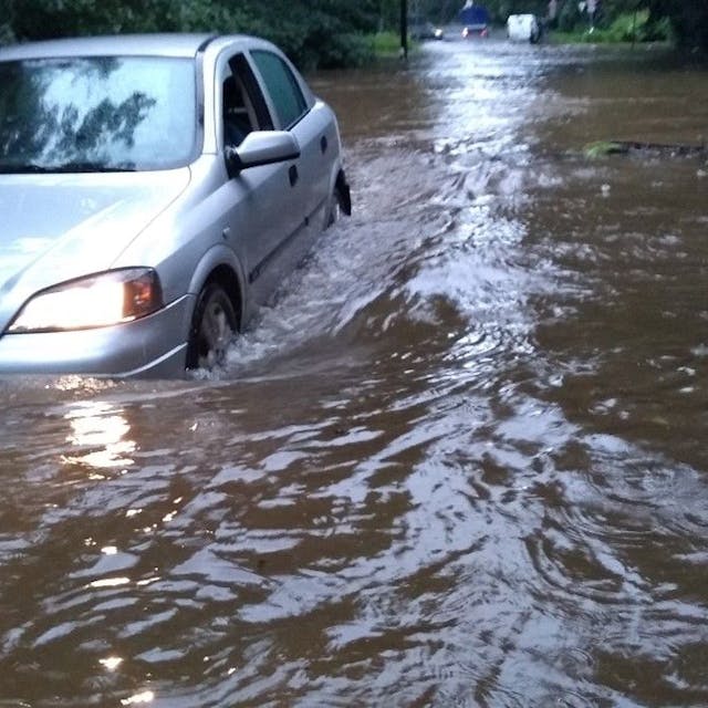 Ein Auto steckt im Hochwassers in Dünnwald fest. Die gesamte Straße ist voller Wasser, es steht dem Auto bis zu den Lichtern.