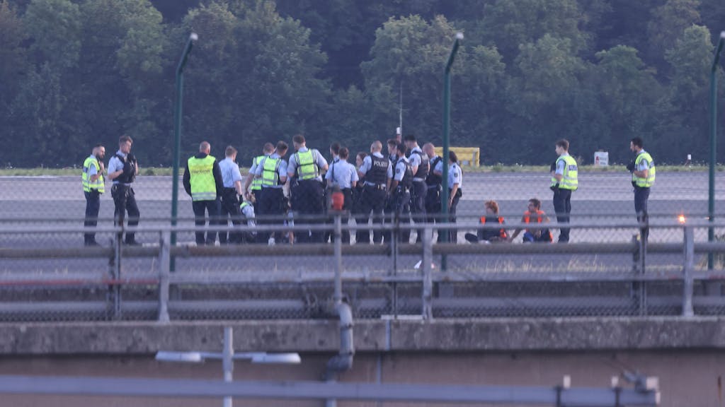 Polizisten stehen am 13. Juli 2023 auf dem Flugfeld des Airports in Düsseldorf und versuchen, Aktivistinnen und Aktivisten der Gruppe „Letzte Generation“ vom Asphalt zu lösen, nachdem sie sich festgeklebt haben.