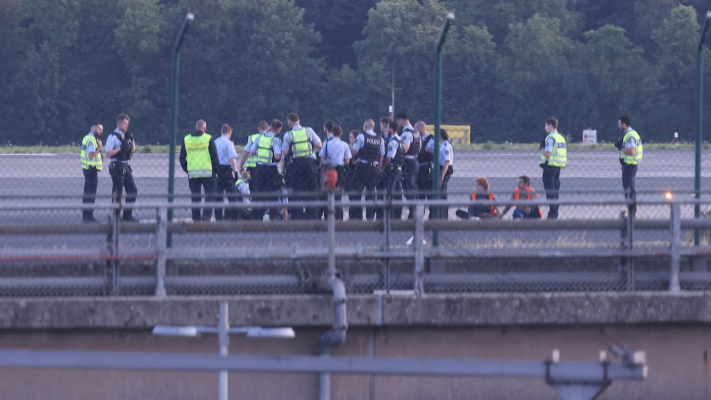 Polizisten stehen am 13. Juli 2023 auf dem Flugfeld des Airports in Düsseldorf und versuchen, Aktivistinnen und Aktivisten der Gruppe „Letzte Generation“ vom Asphalt zu lösen, nachdem sie sich festgeklebt haben.