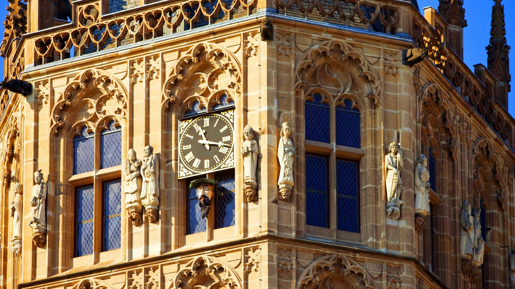 Auf dem Bild zu sehen ist das oberste Stockwerk des Rathausturms, an der eine Uhr und einige Steinskulpturen angebracht sind.