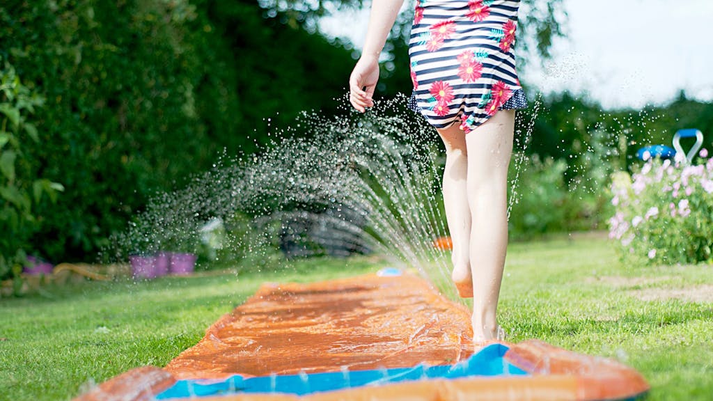Ein Mädchen spielt mit einer Wasserrutsche im Garten.