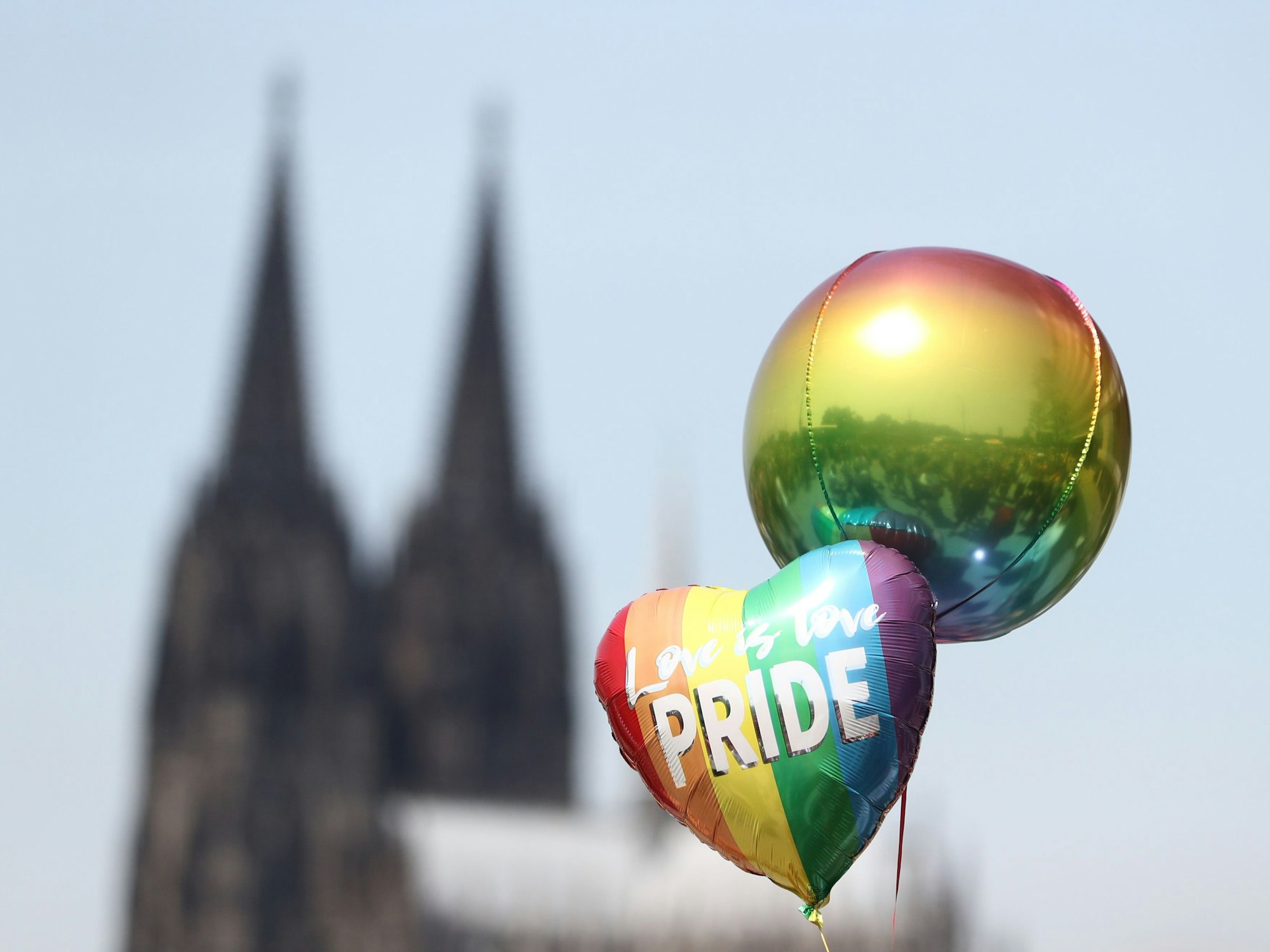 Zwei Ballons, einer in Herzform, schweben in der Luft, im Hintergrund ist der Kölner Dom.