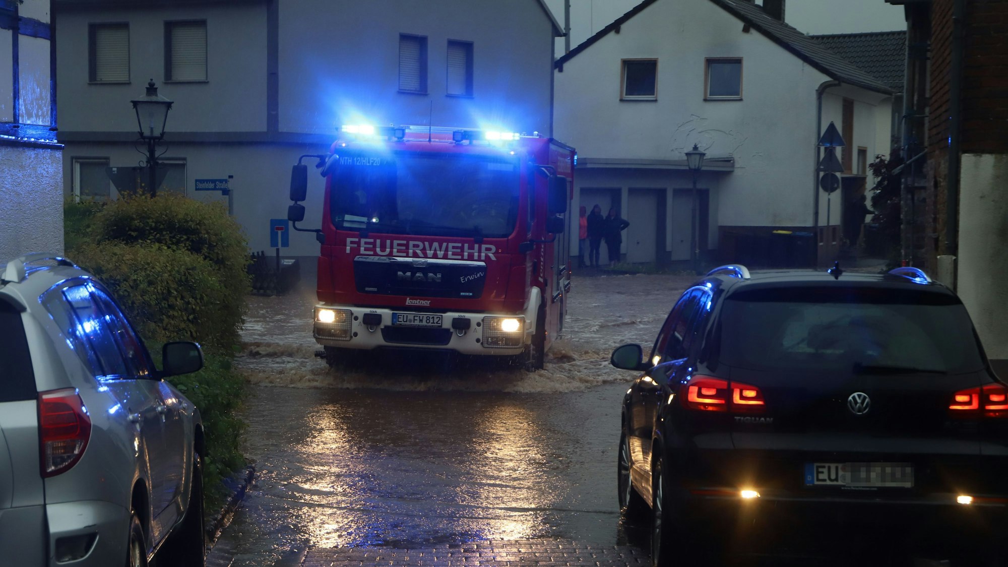 Ein Feuerwehrauto fährt mit Blaulicht über eine überflutete Straße.