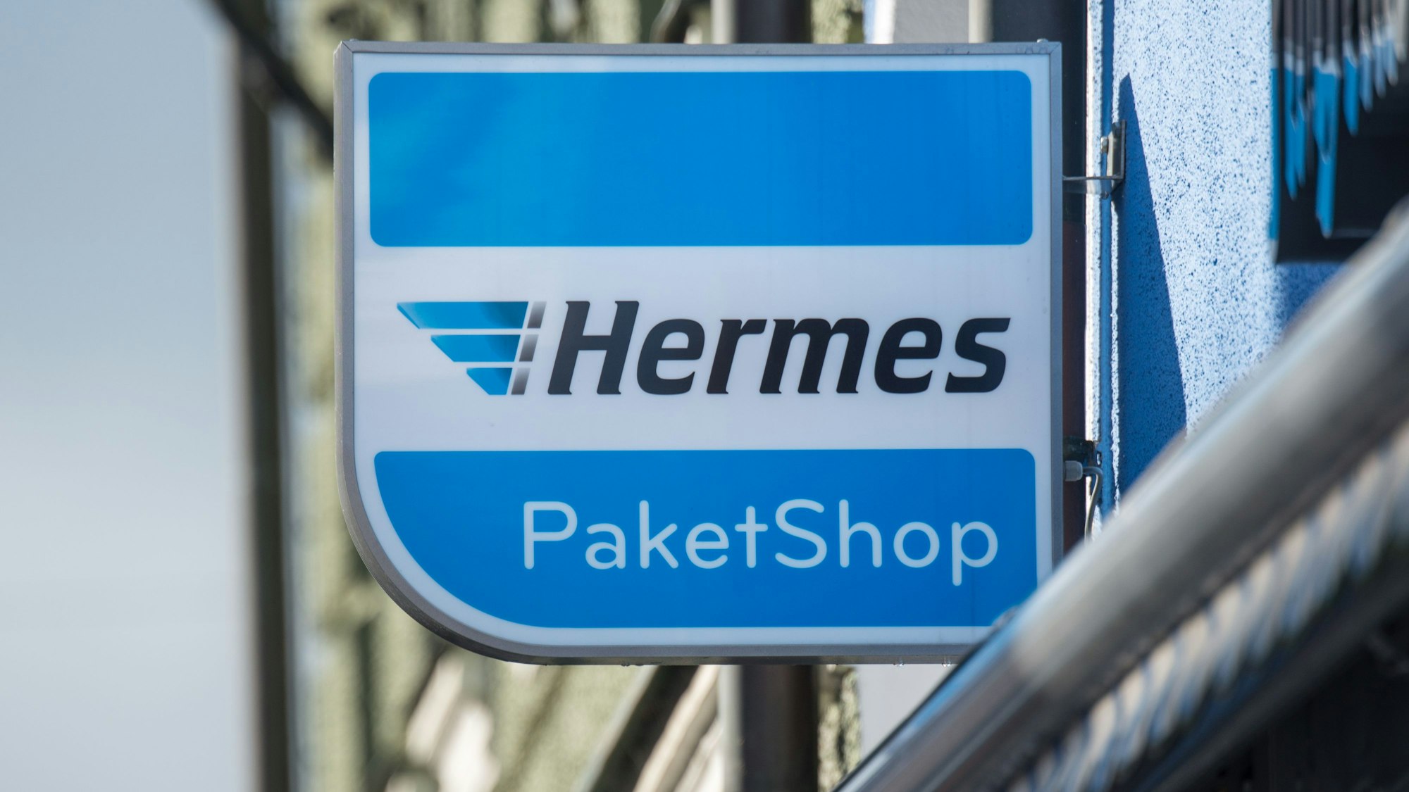 Ein Schild mit der Aufschrift „Hermes Paket Shop“ ist vor einem Geschäft angebracht.