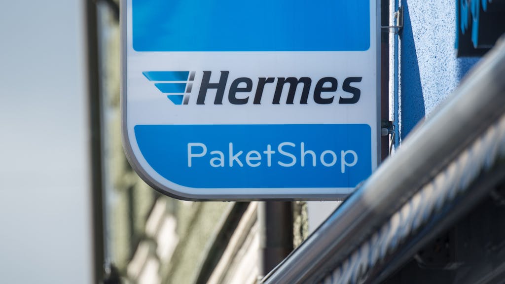 Ein Schild mit der Aufschrift „Hermes Paket Shop“ ist vor einem Geschäft angebracht.