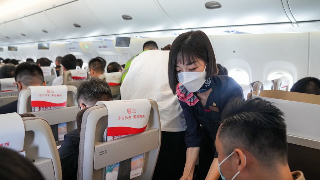 Eine Flugbegleiterin serviert einem Passagier an Bord eine Mahlzeit.