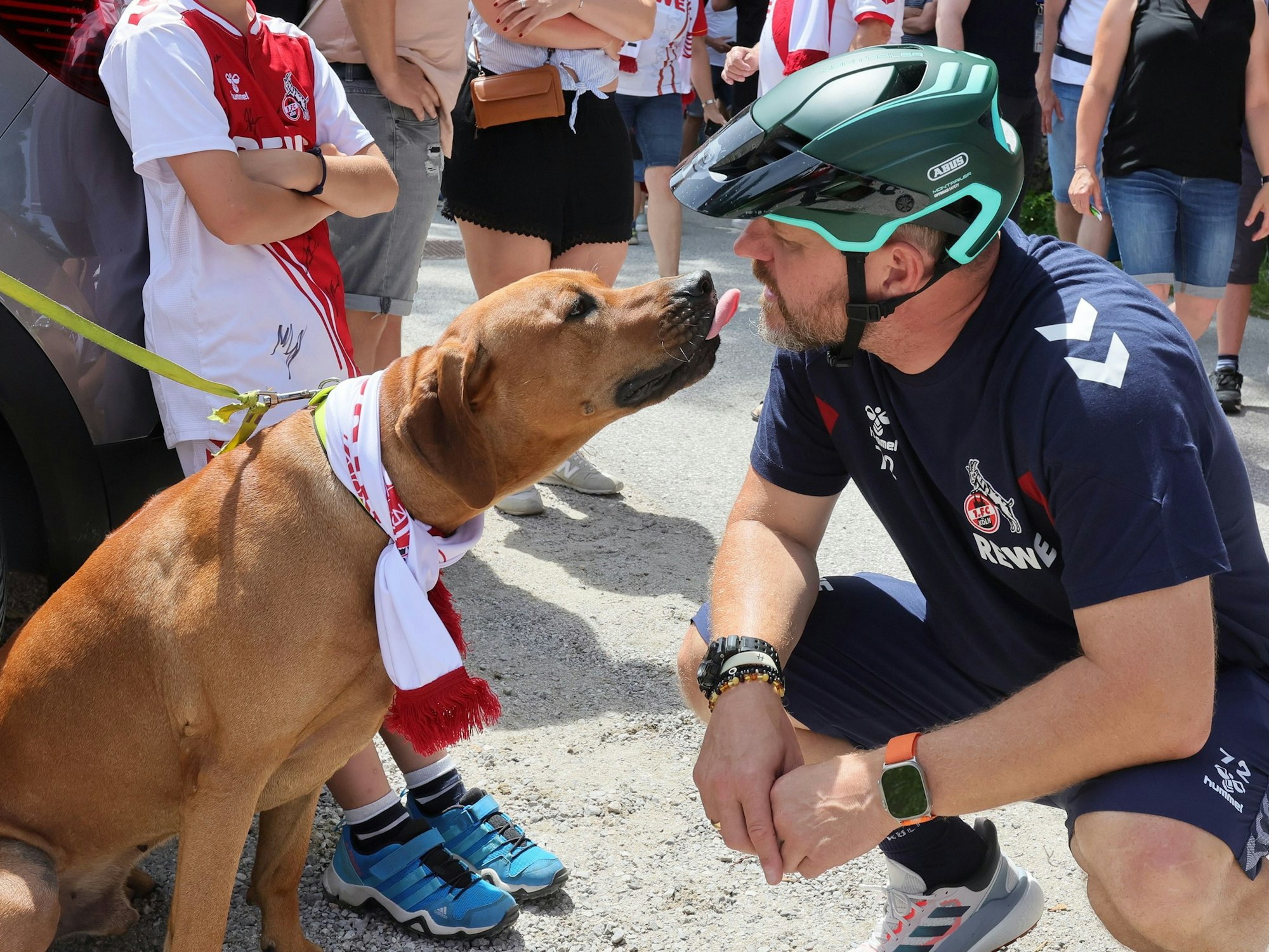 Steffen Baumgart und ein Hund mit Fanschal freunden sich an.