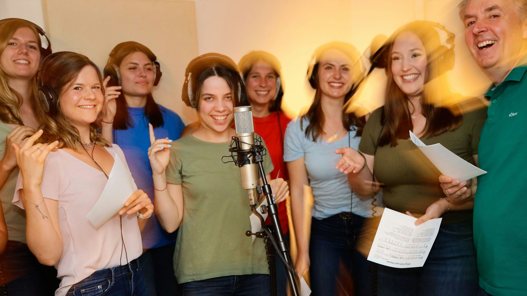 Sieben Sängerinnen vom Chor und der Chorleiter stehen im Studio und nehmen ein Lied auf.