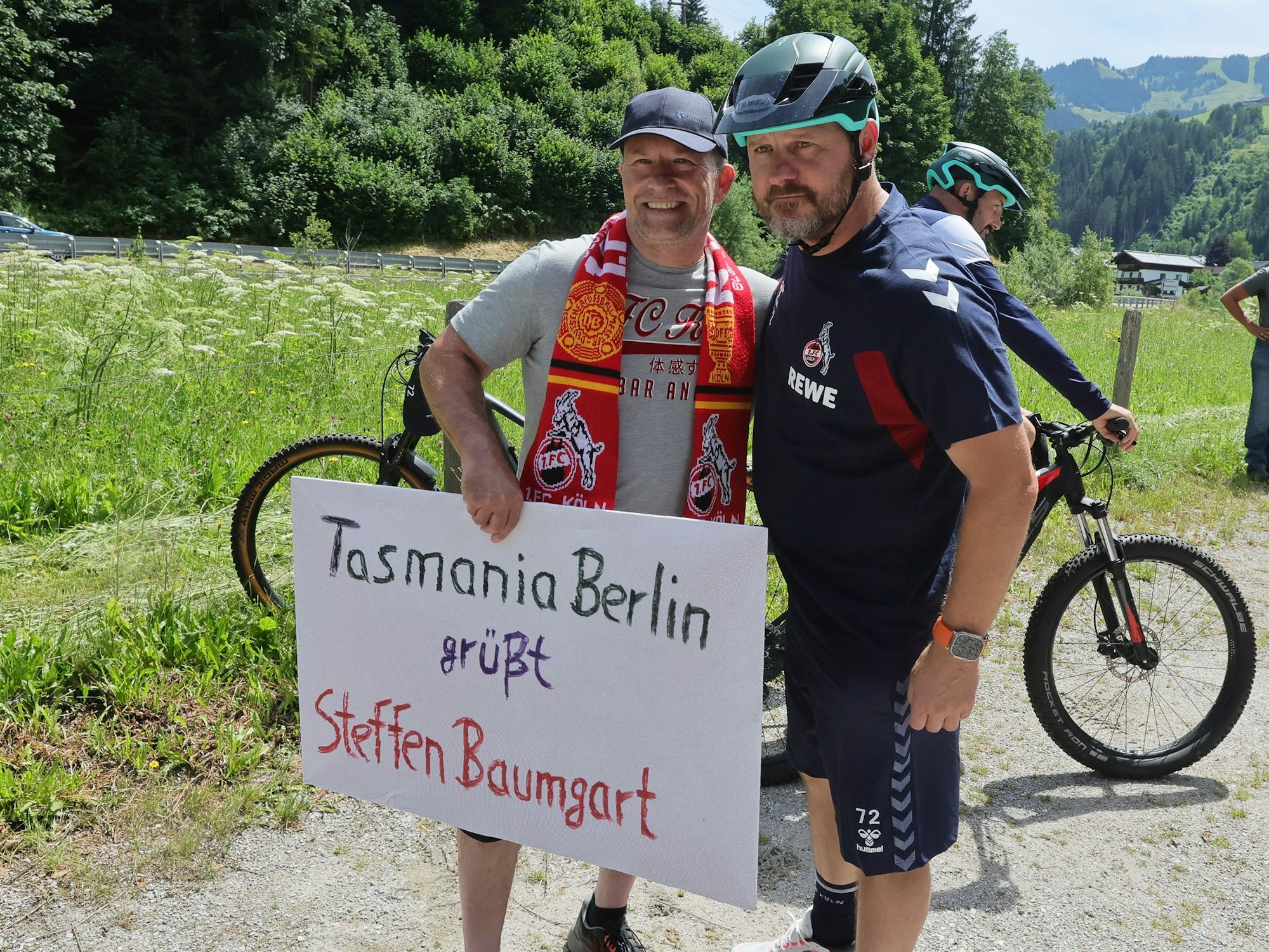 Der FC-Trainer posiert mit einem Fan, der ein Schild mit der Aufschrift „Tasmania Berlin grüßt Steffen Baumgart“ in die Kamera hält.