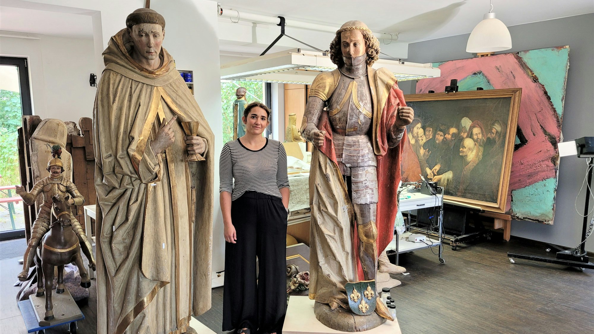 Eine Frau steht zwischen zwei großen Heiligenfiguren in einem Atelier.