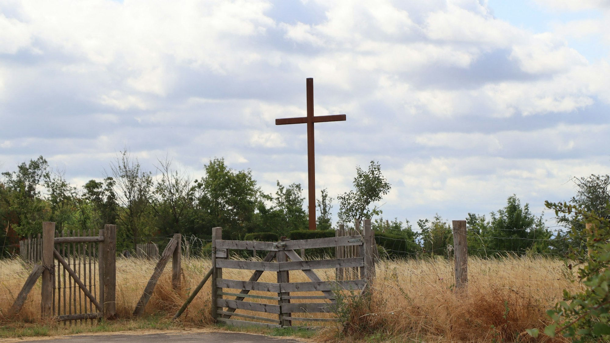 Hinter einem Weidezaun steht ein großes Holzkreuz.
