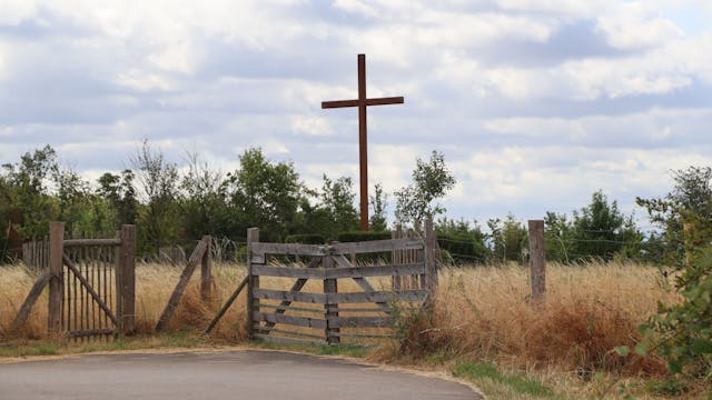 Hinter einem Weidezaun steht ein großes Holzkreuz.