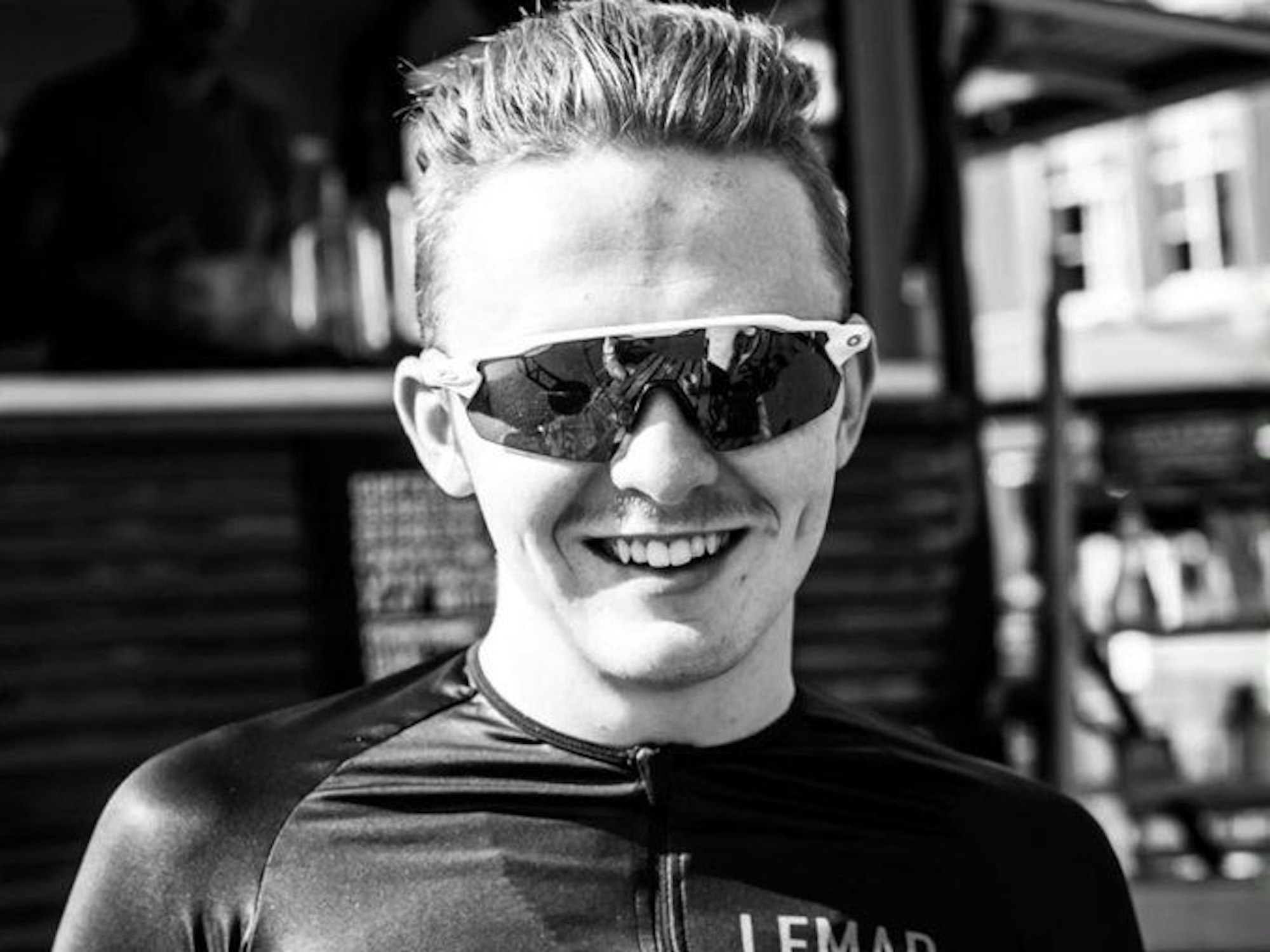 Connor Lambert lacht auf einem Schwarz-Weiß-Bild mit Sonnenbrille in die Kamera.