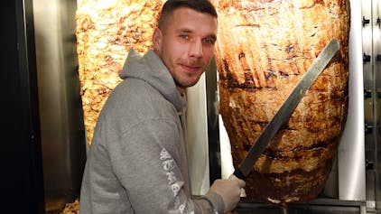 Fußball-Weltmeister Lukas Podolski steht bei der Eröffnung eines Döner-Ladens an einem Dönerspieß.