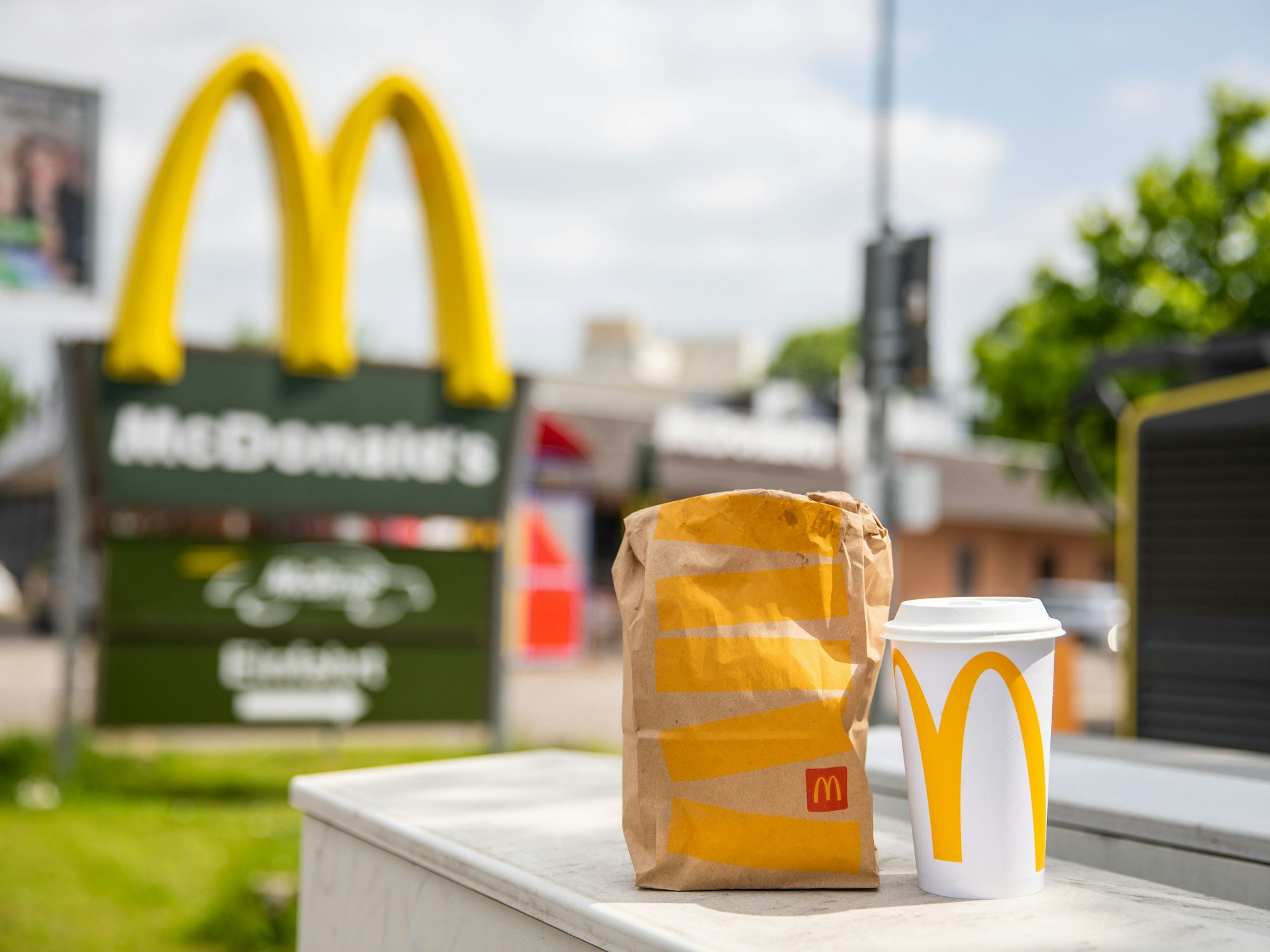Eine McDonald's-Tüte und ein dazugehöriger To-Go-Becher stehen vor einer McDonald's-Filiale.