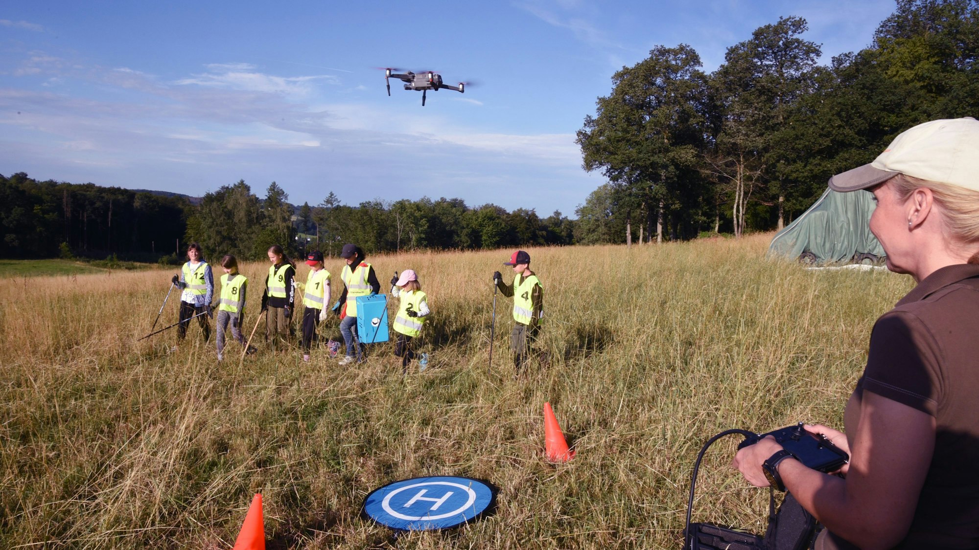 Jugendliche suchen im Gras nach Rehkitzen, eine Drohne mit Wärmebildkamera hilft bei der Suche.