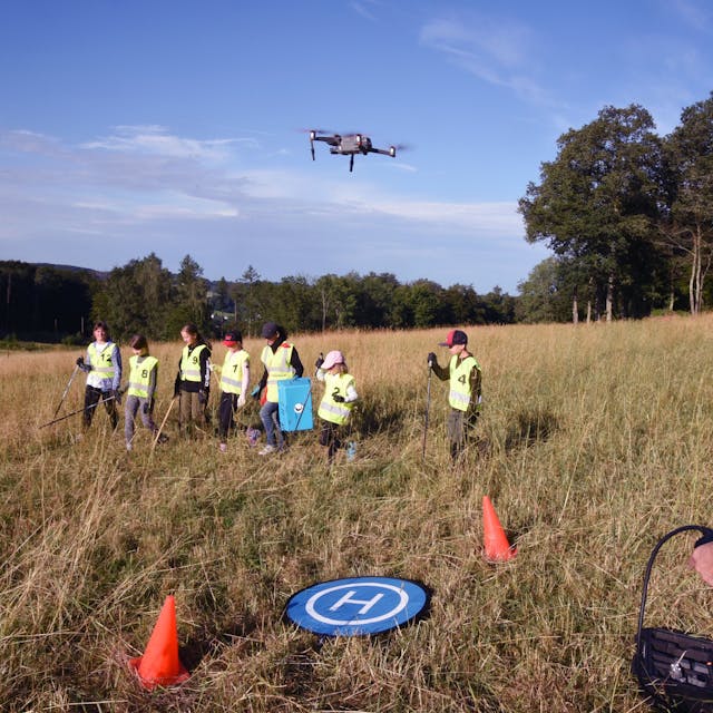Jugendliche suchen im Gras nach Rehkitzen, eine Drohne mit Wärmebildkamera hilft bei der Suche.