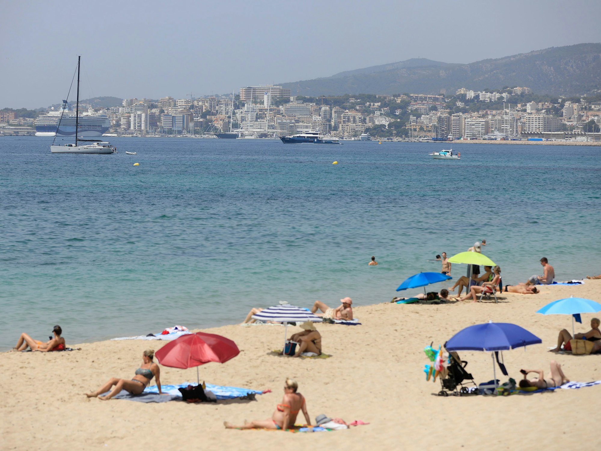 Menschen sonnen sich und benutzen Sonnenschirme am Strand Can Pere Antoni in Palma de Mallorca.
