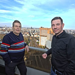 Zwei Männer auf einem Balkon, im Hintergrund sieht man die Skyline von Köln.