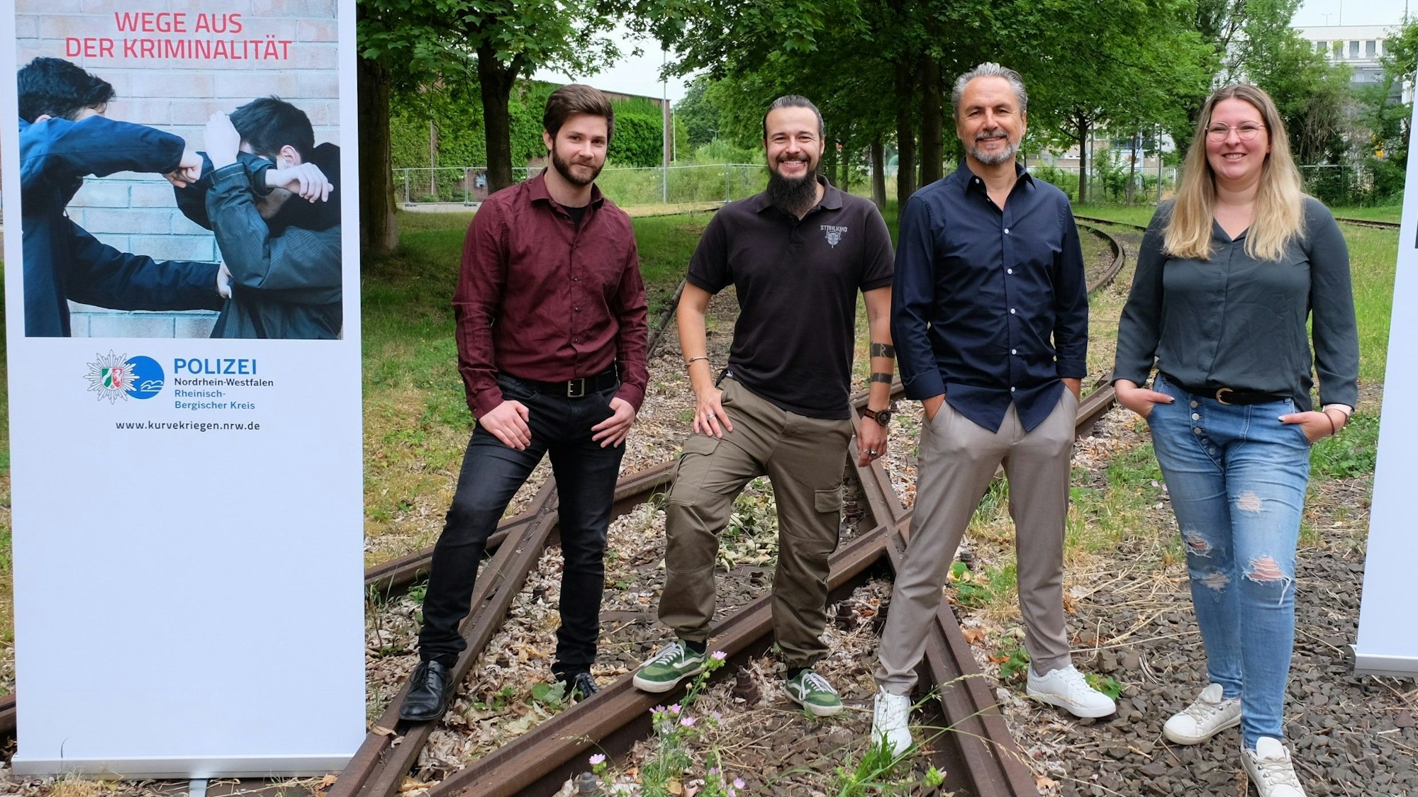 Das Team "Kurve kriegen" im Rheinisch-Bergischen Kreis: Tizio Fata, Timo König, Stefan Lurz, Lea Dörwaldt stehen mit Plakate auf Bahngleisen.