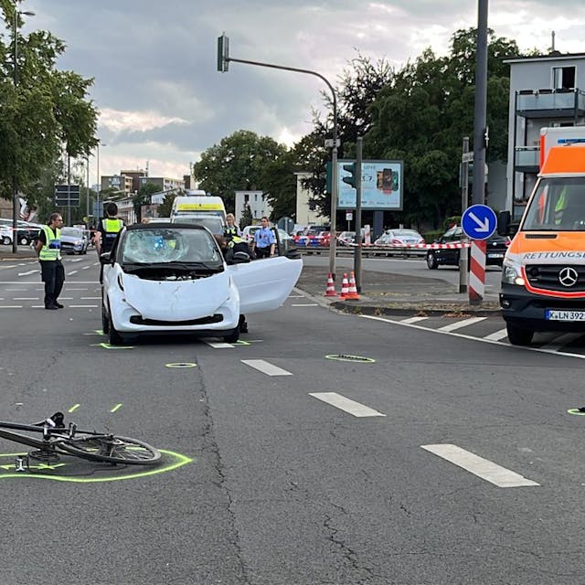 Unfallort mit einem demonlierten Auto, einem auf dem Boden liegenden Fahrrad und einem Krankenwagen