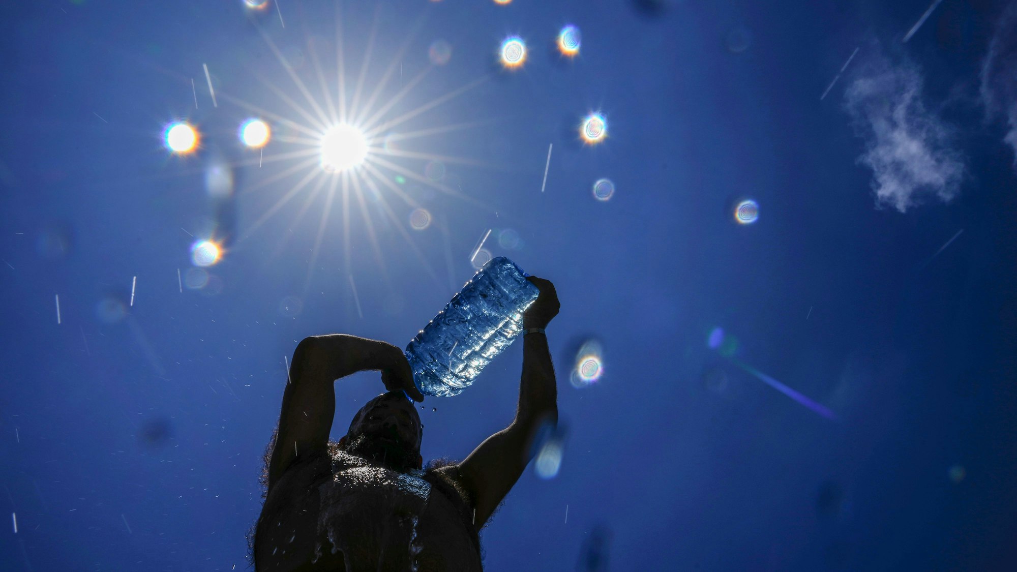 Ein Mann gießt sich kaltes Wasser über den Kopf, um sich an einem drückend heißen Tag abzukühlen