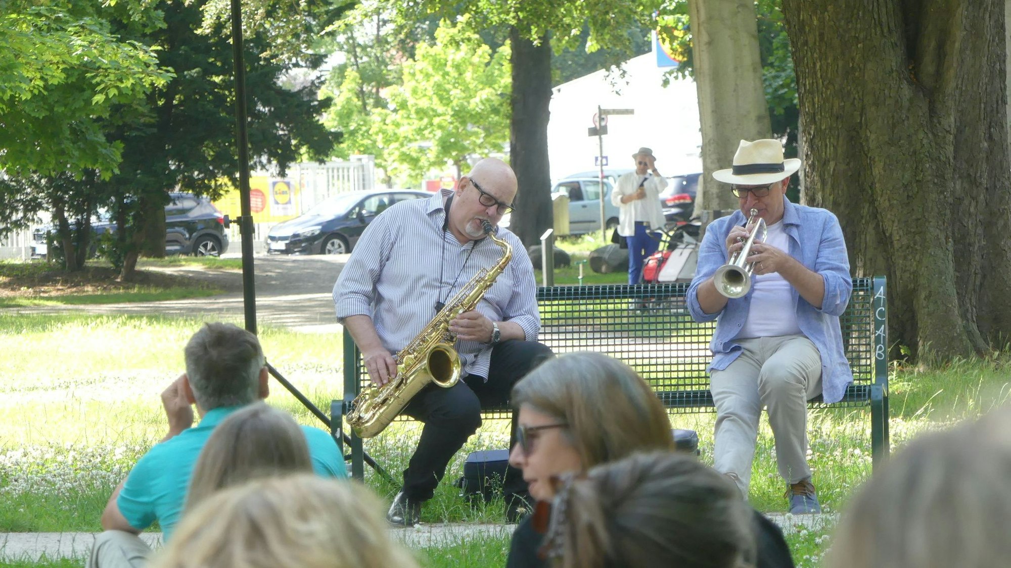 Bernd Delbrügge und Ebasa Pallada spielen auf einer Parkbank Saxofon und Trompete.
