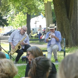 Bernd Delbrügge und Ebasa Pallada&nbsp; spielen auf einer Parkbank Saxofon und Trompete.