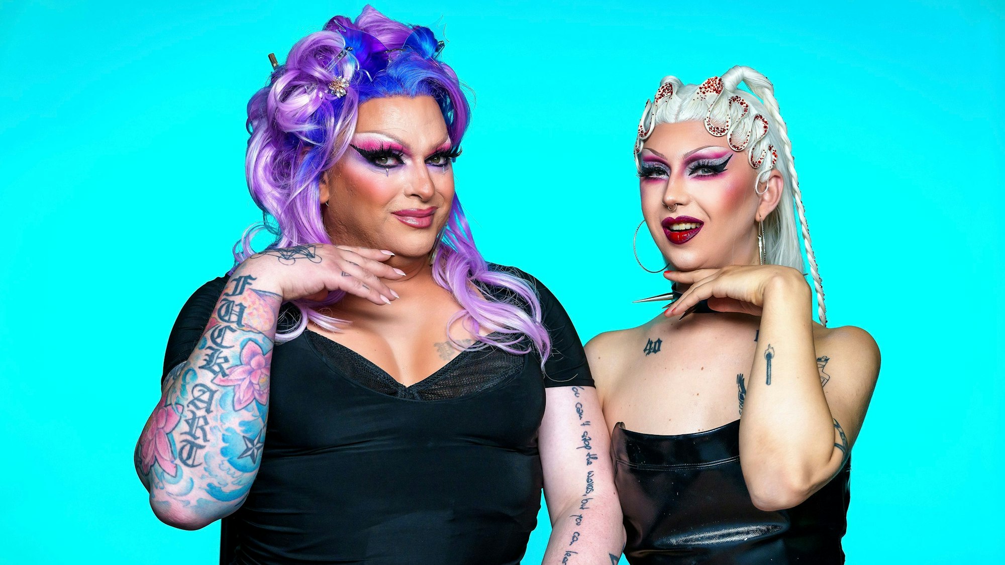 Die beiden Drag Queens posieren für die Kamera. Barbie Breakout hat auffällig violette Haare, beide sind geschminkt und tragen schwarze Kleidung.