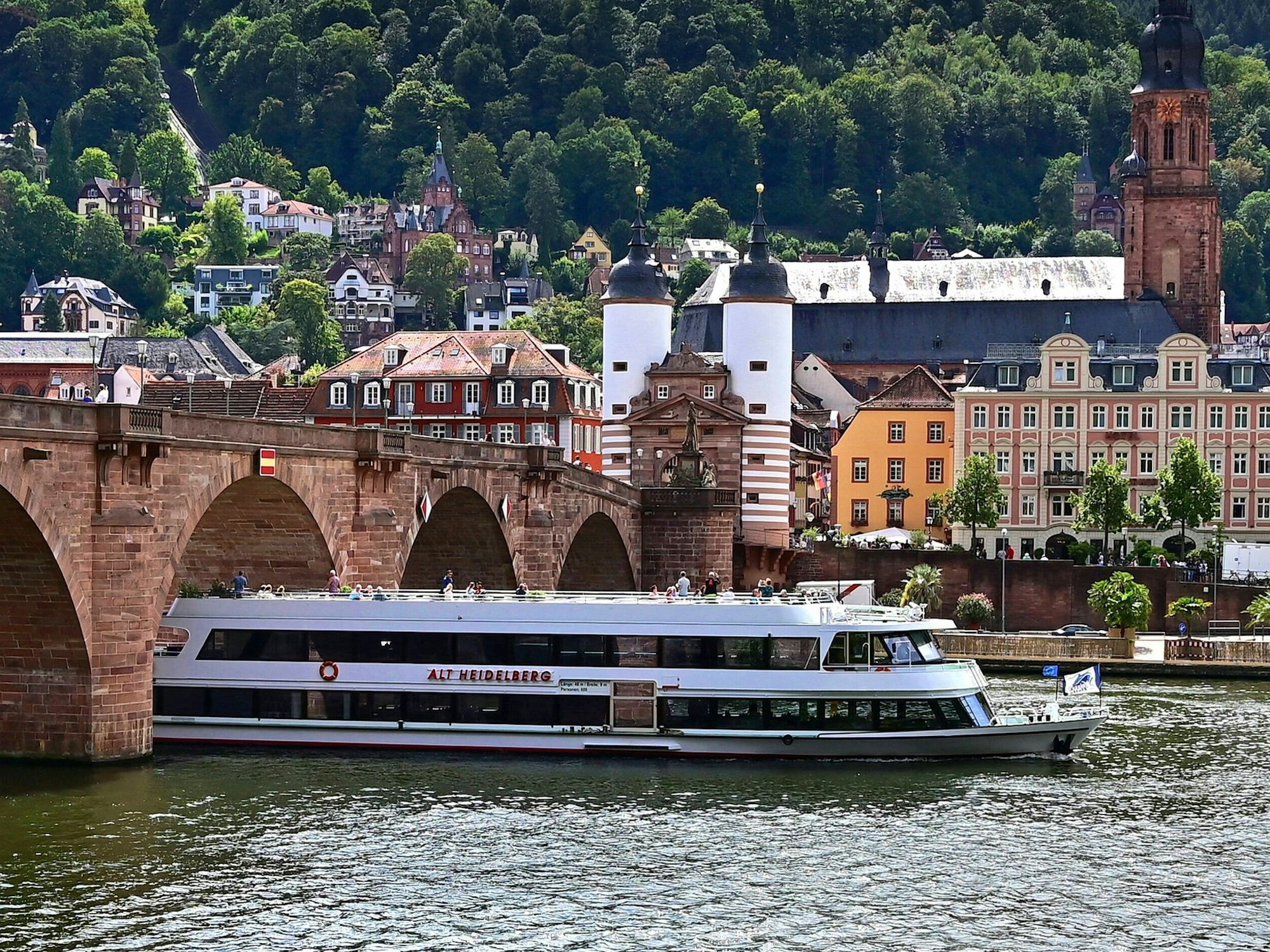 Die alte Brücke und das Schloss in Heidelberg am Neckar. Ein Schiff fährt im Vordergrund vorbei.