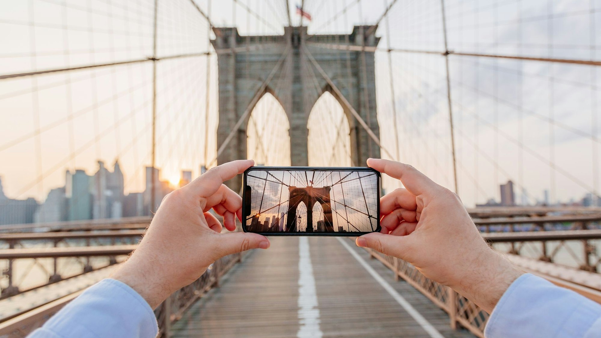 Ein Tourist fotografiert die Brooklyn Bridge mit dem Smartphone.