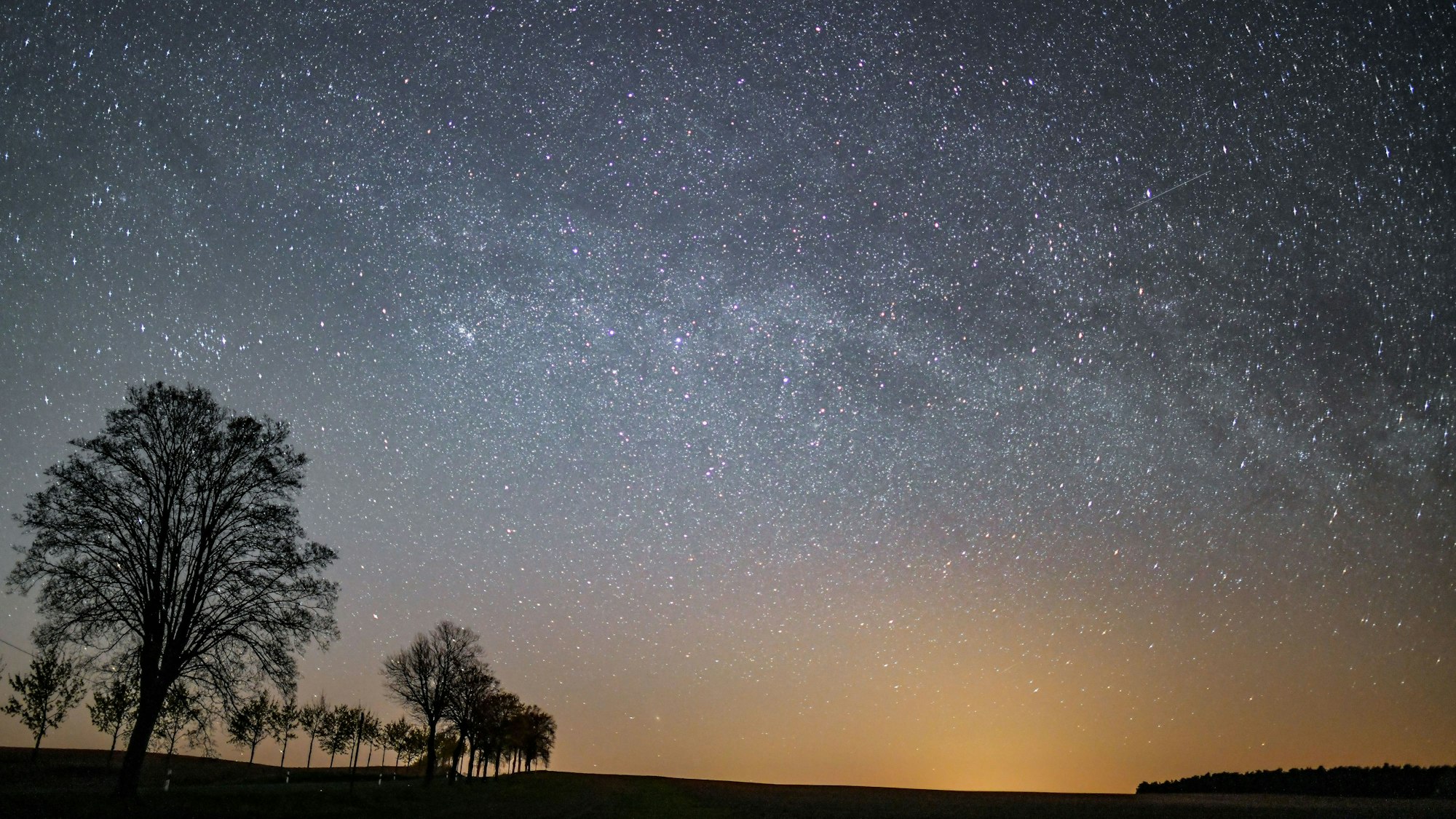 Der Sternenhimmel leuchtet in der Nacht über der Landschaft.