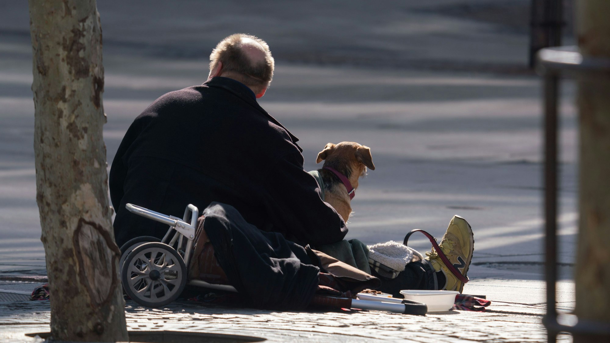 Ein Mann sitzt mit seinem Hund an der Straße.
