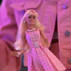 Barbie-Puppe vor einer rosa Jeansjacke mit Barbie-Logo