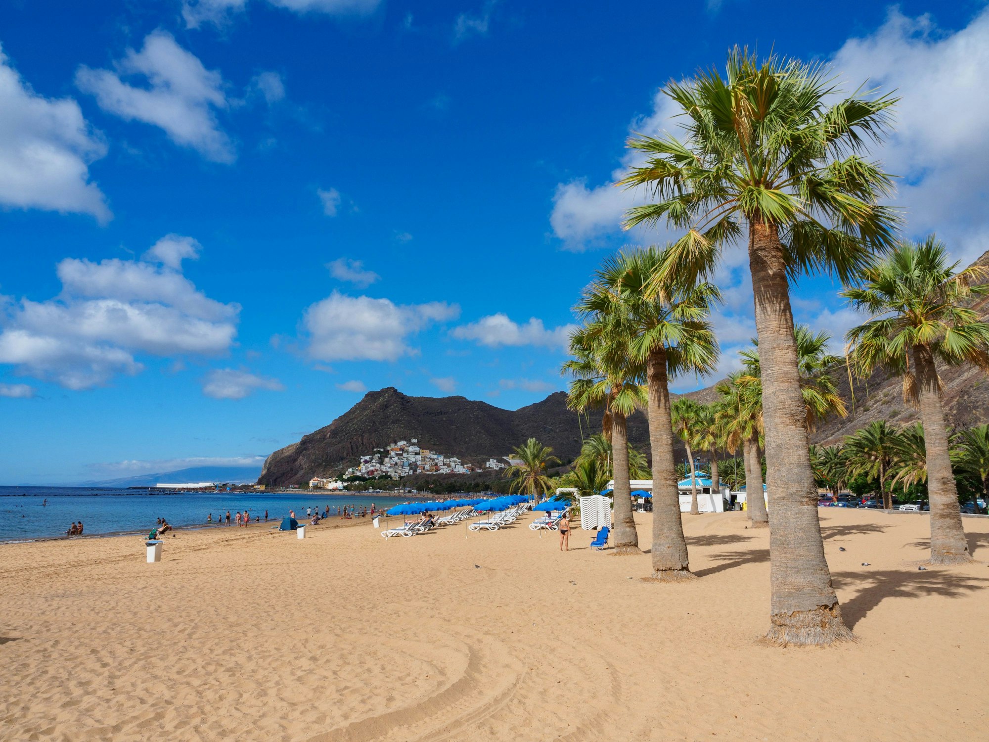 Sonnenschirme sowie Urlauberinnen und Urlauber liegen am Playa de Las Teresitas auf Teneriffa in Spanien. Der Strand zählt zu den besten preiswerten Stränden in Europa.